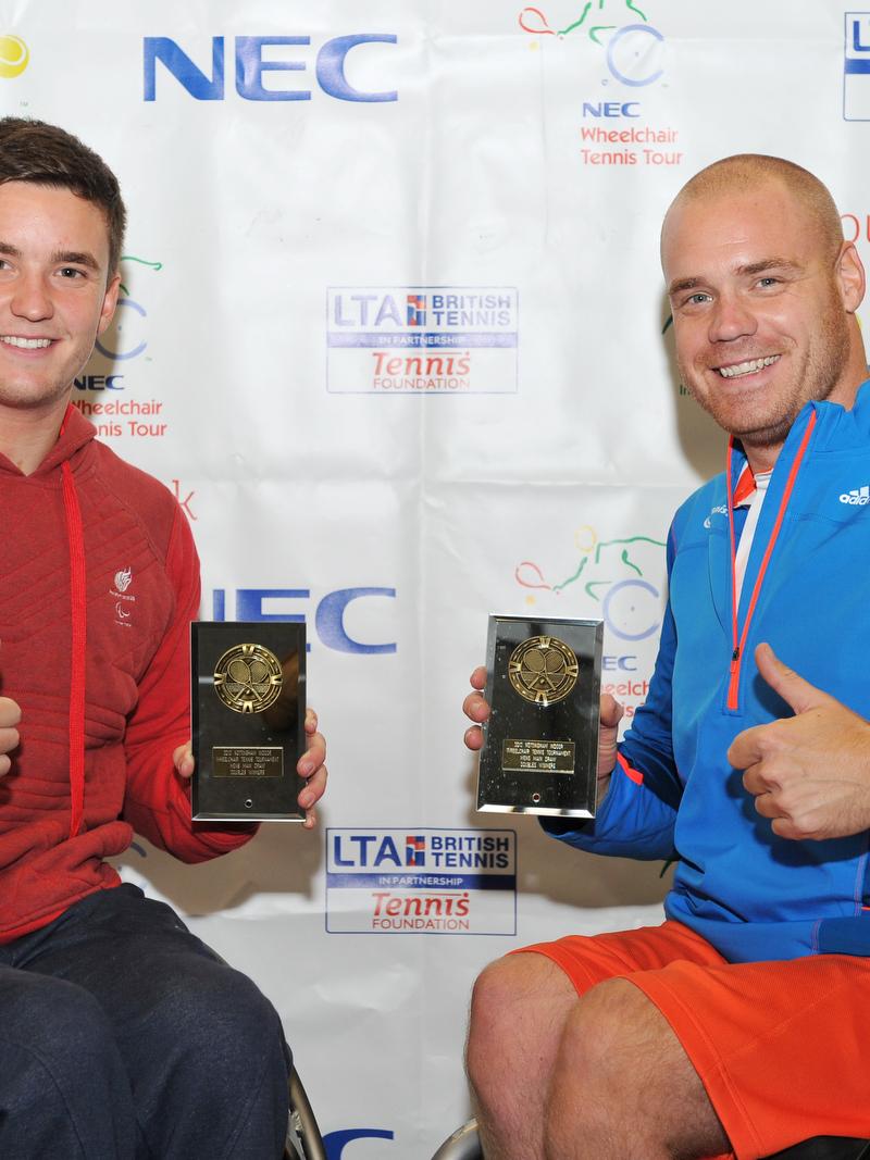 A picture of 2 men in a wheelchair showing their trophies