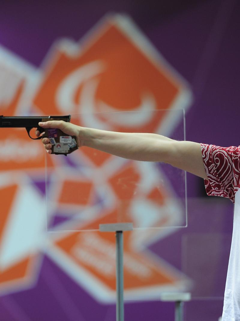 Sergey Malyshev of Russia, wearing glasses, a visor and ear protection shoots his Mixed P3-25m Pistol at an indoor range at The Royal Artillery Barracks
