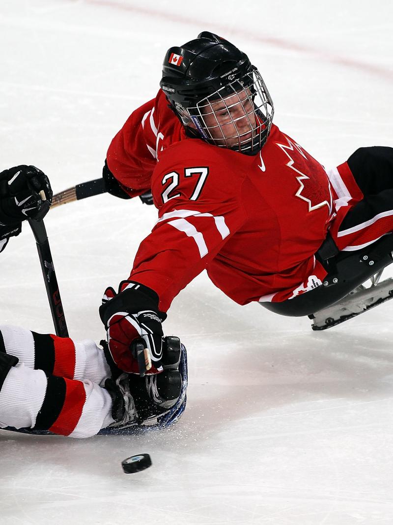 A picture of a 2 men in a sldege playing hockey
