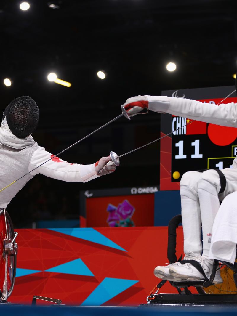 A picture of 2 men in wheelchairs fencing.