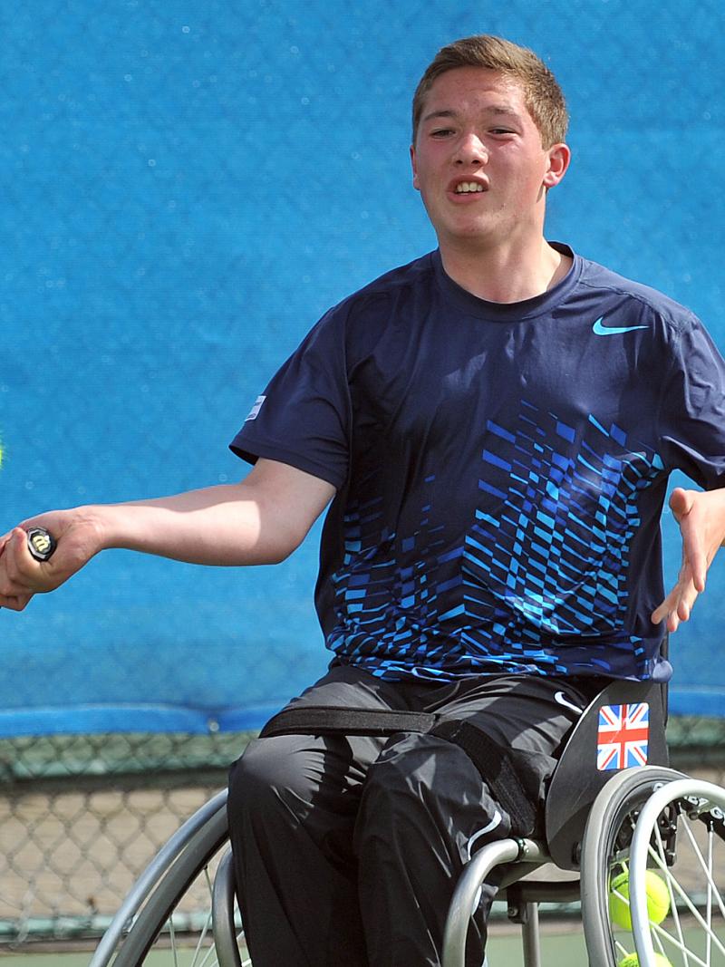 A picture of a young man in a wheelchair playing a forhand in a wheelchair tennis match