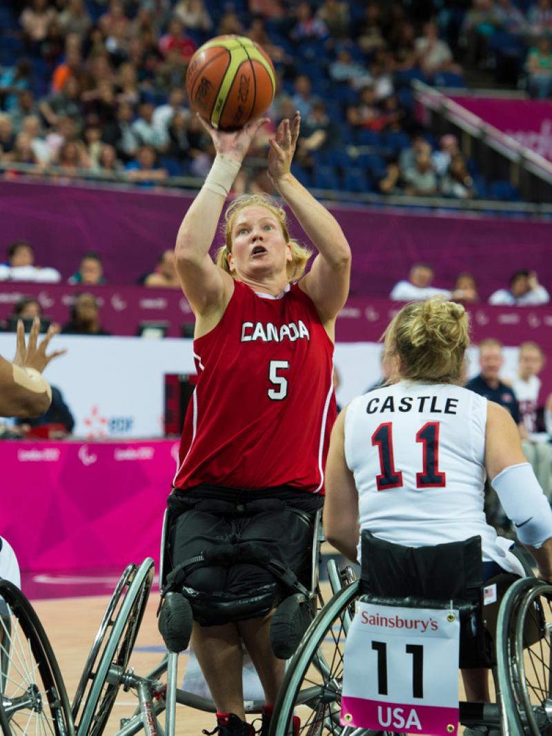 A picture of a woman in a wheelchair shooting between two defenders during a wheelchair basketball match.