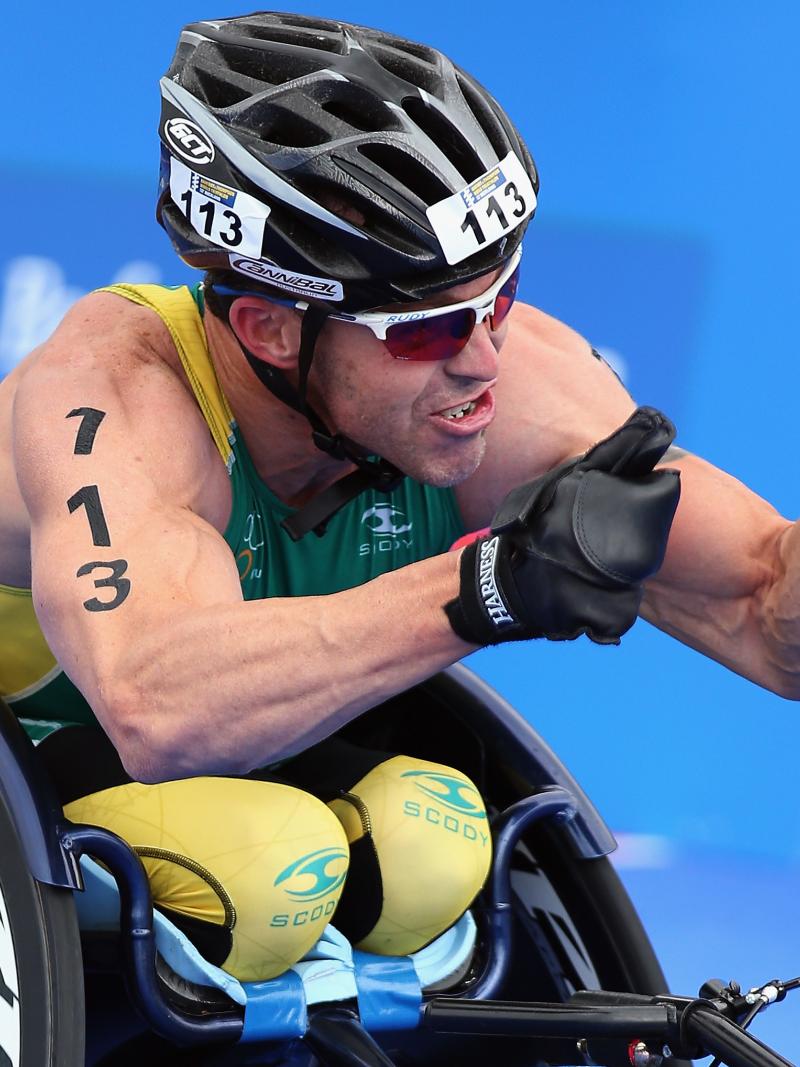 A picture of a man in a wheelchair celebrating his victory after a para-triathlon