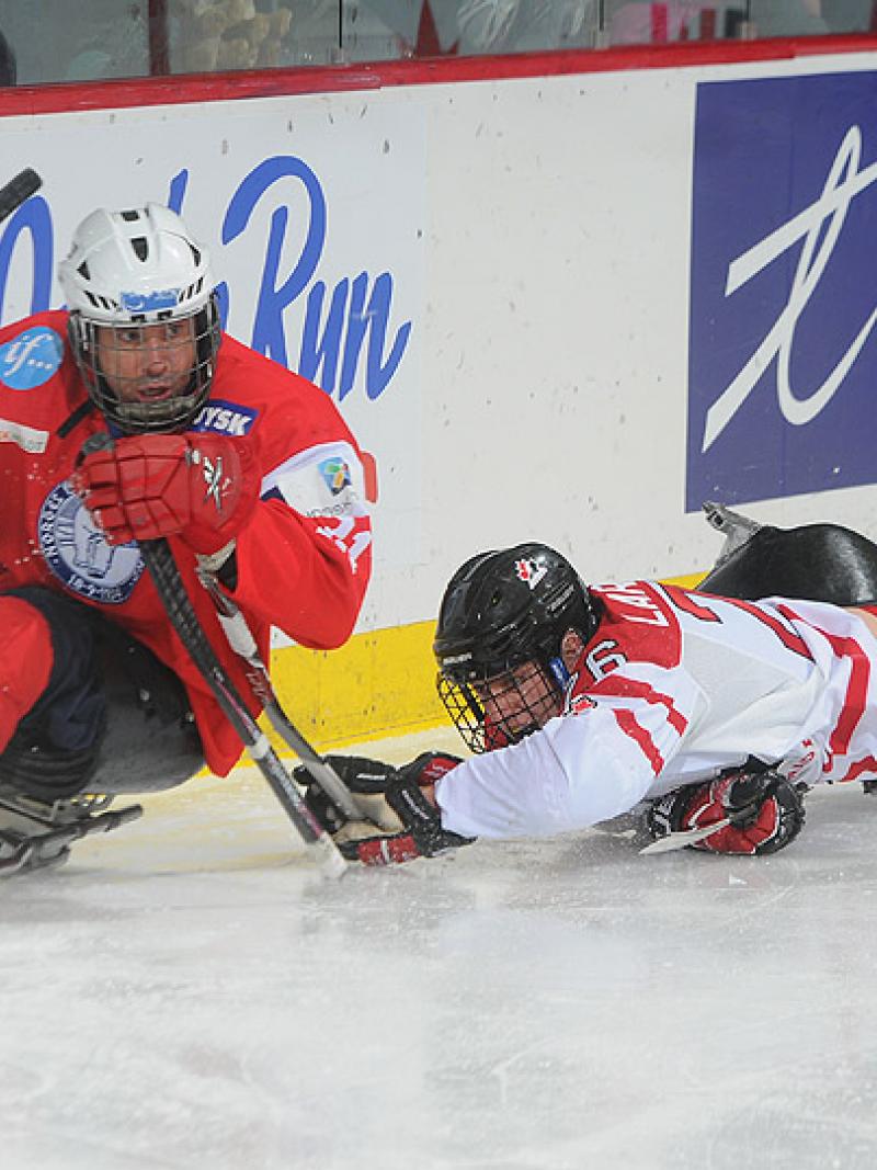 A picture of two men in a sledge playing ice sledge hockey.
