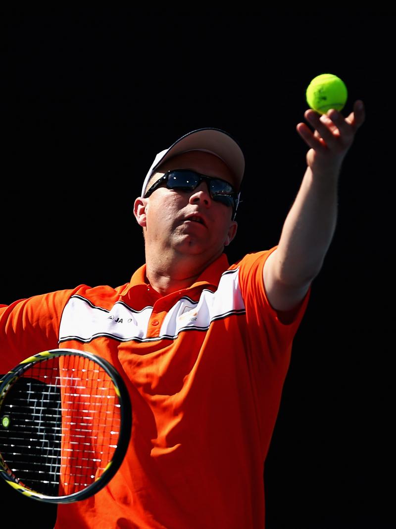 A picture of a man in a wheelchair serving during a tennis match