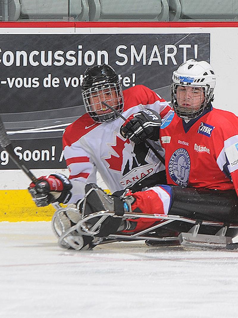 A picture of a two men in sledges playing ice hockey