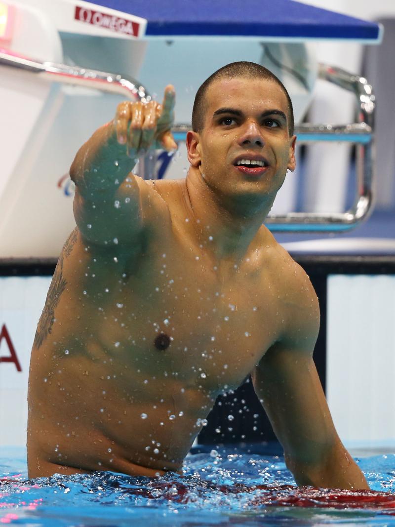 A picture of a man in the pool sitting on the swimming line with his hand up 