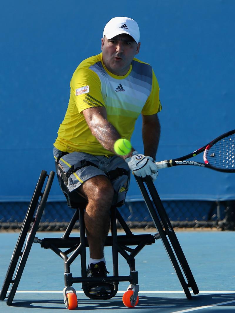 A picture of a man in a wheelchair playing a backhand during a wheelchair tennis match