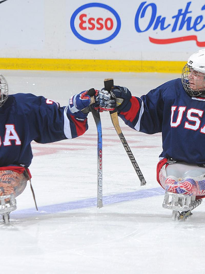 A picture of 2 mens in sledges during an ice sledge hockey match