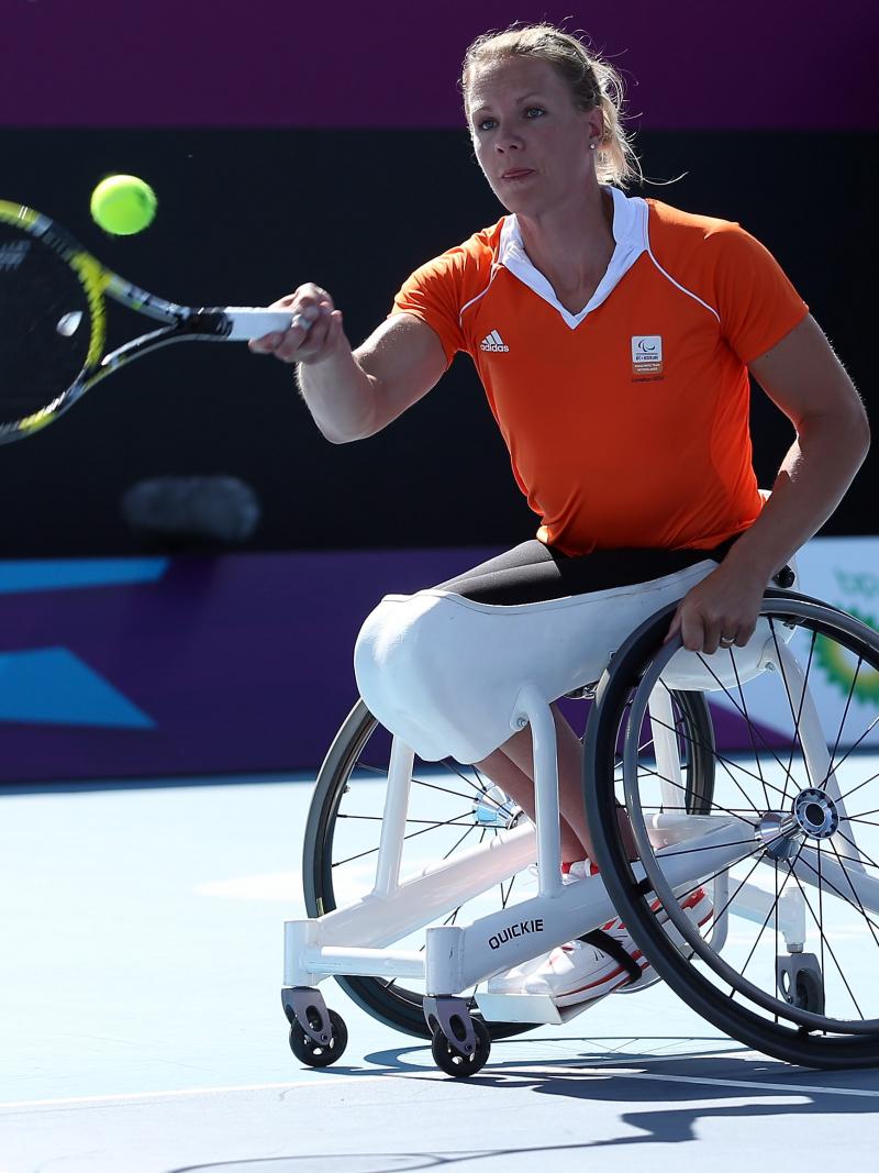 A picture of a woman in a wheelchair playing a forhand during a wheelchair tennis match.