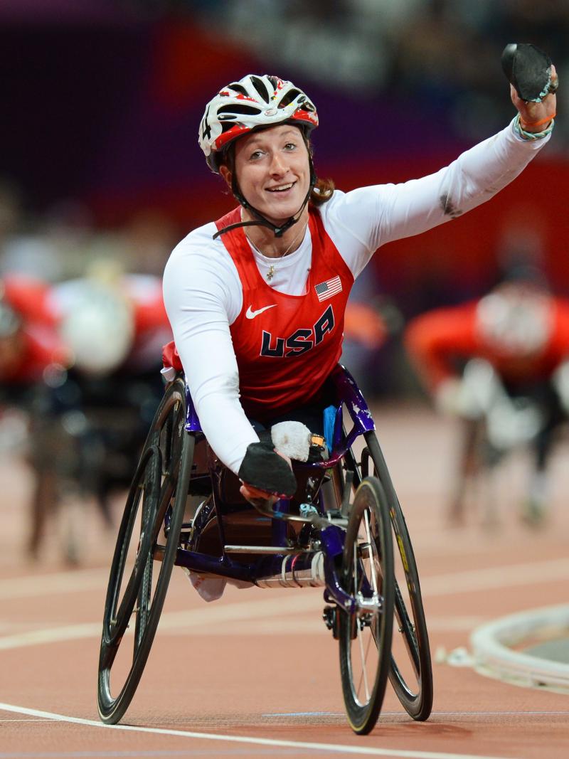 A picture of a woman in the wheelchair on a track celebrating with her hand up