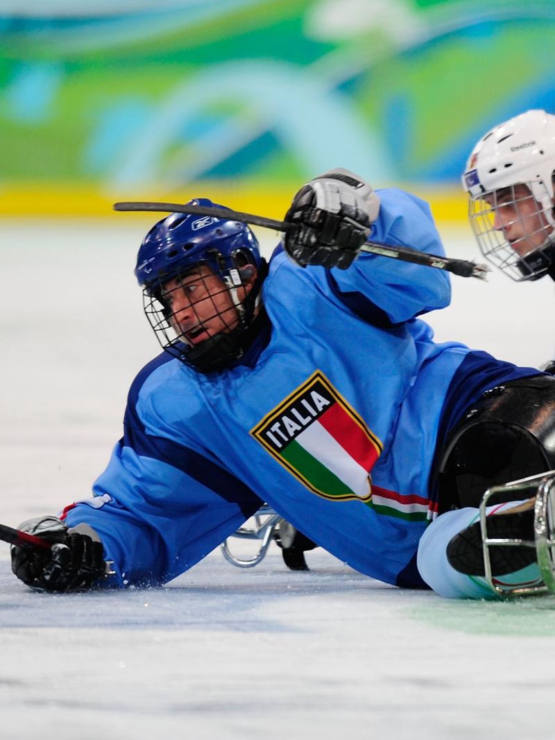 A picture of two men in sledges fighting the puck during a ice sledge hockey match