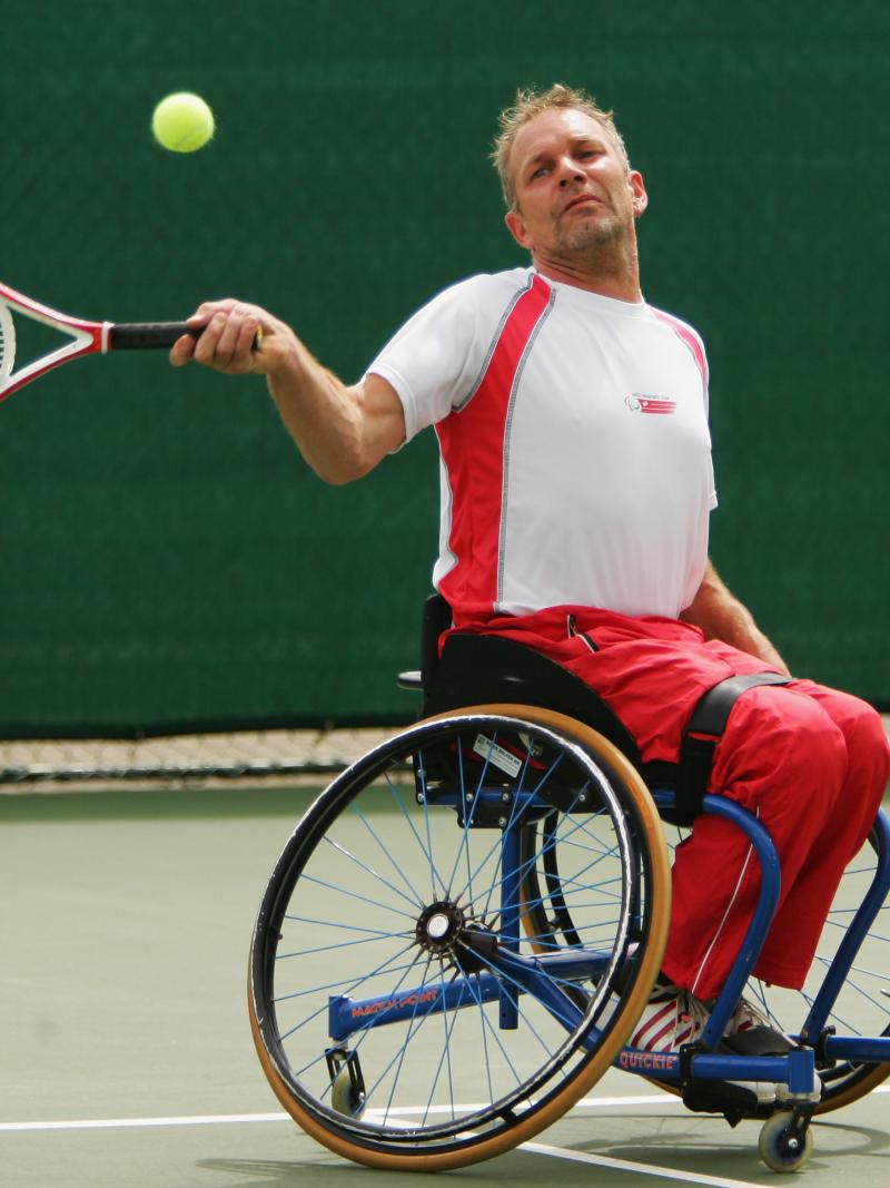 A picture of a man in a wheelchair playing a forehand in a tennis match
