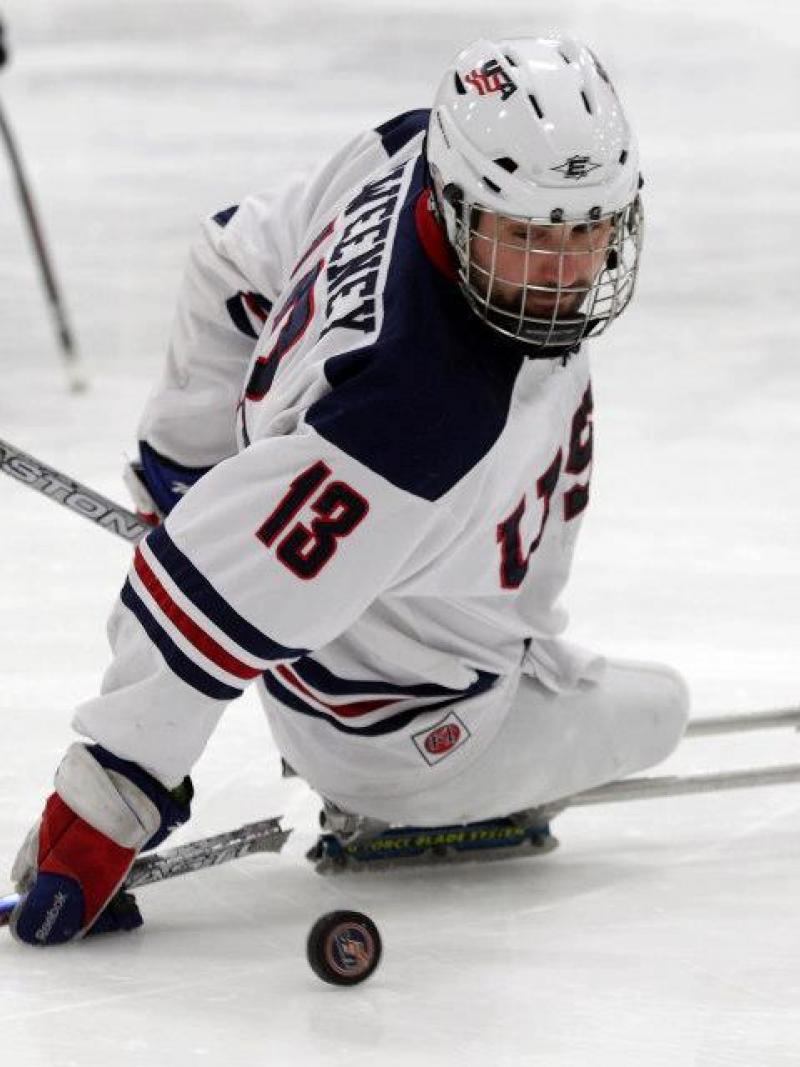 A picture of a man in a sledge playing ice hockey