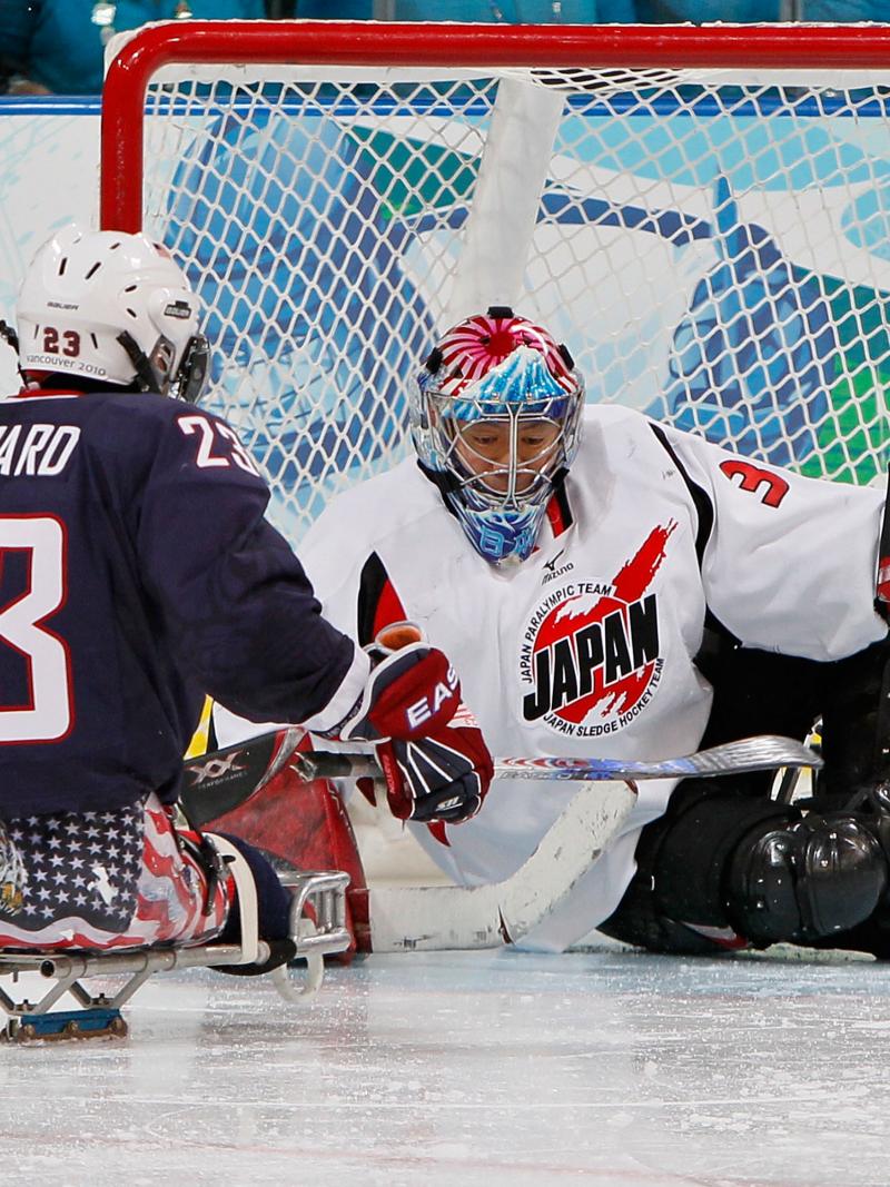A picture of a man in sledge shooting the puck against the goalkeeper in an ice hockey match