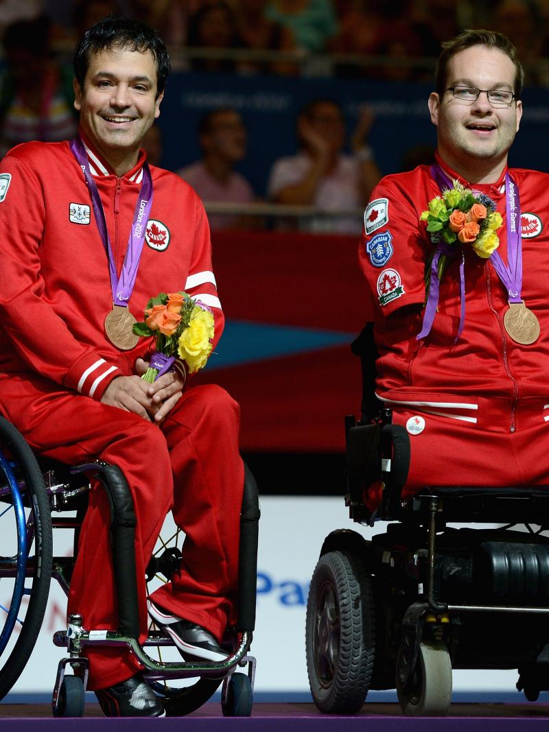 Two boccia player sit in the wheelchairs with their medals around their neck.