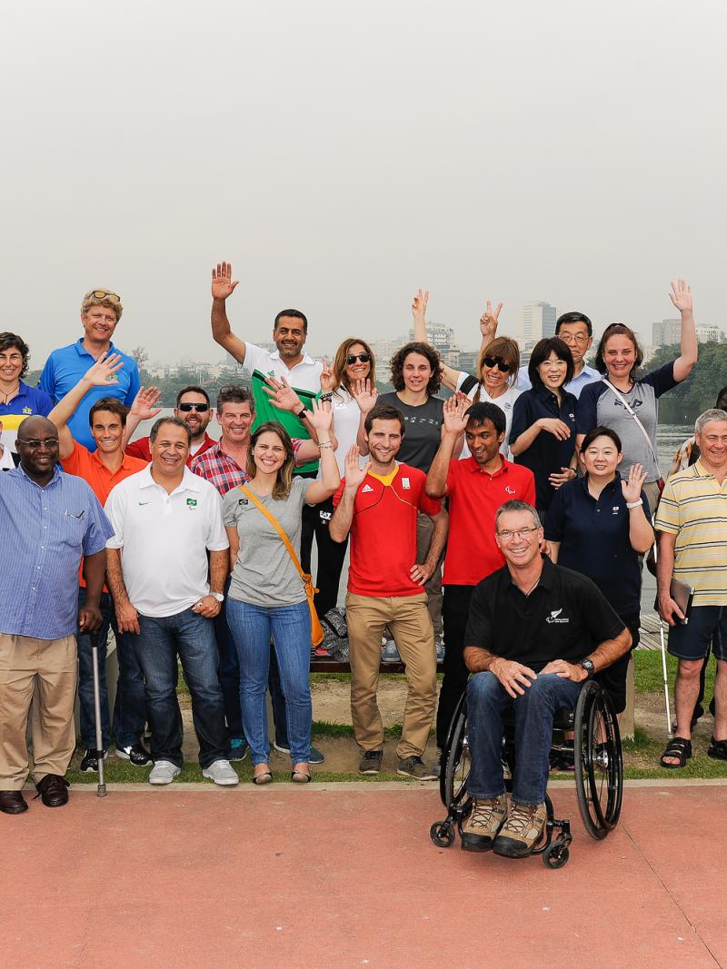 A group of people pose for a photo, waving in front of a body of water.