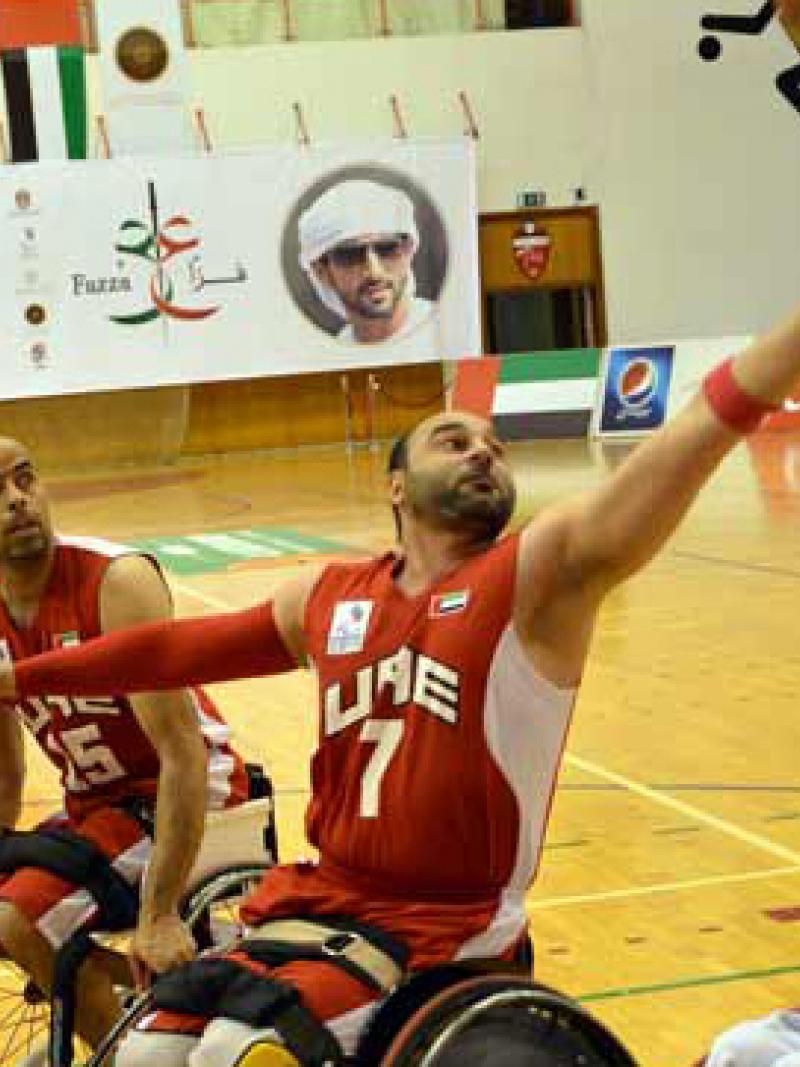 A man in a wheelchair shoots a basketball layup. 