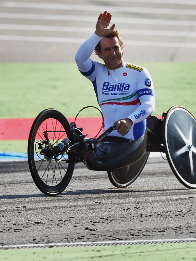 A man in a handcycle waves to spectators from a dirt track.