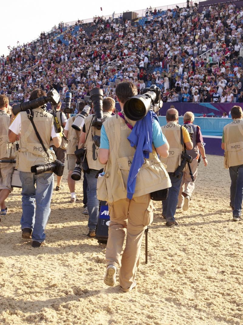 A group of photographers' backs are shown as the walk across an equestrian venue.