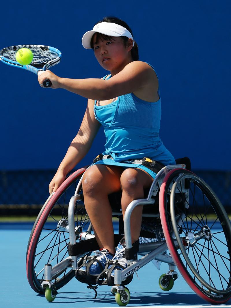 A woman in a wheelchair hits a tennis ball as a backhand.