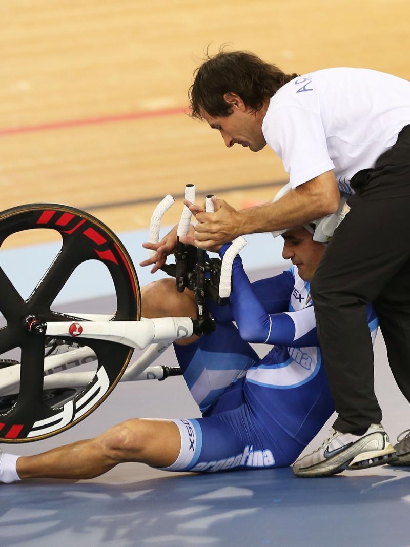 A man sits beside the track trying to get up with his bike with another man assisting him.