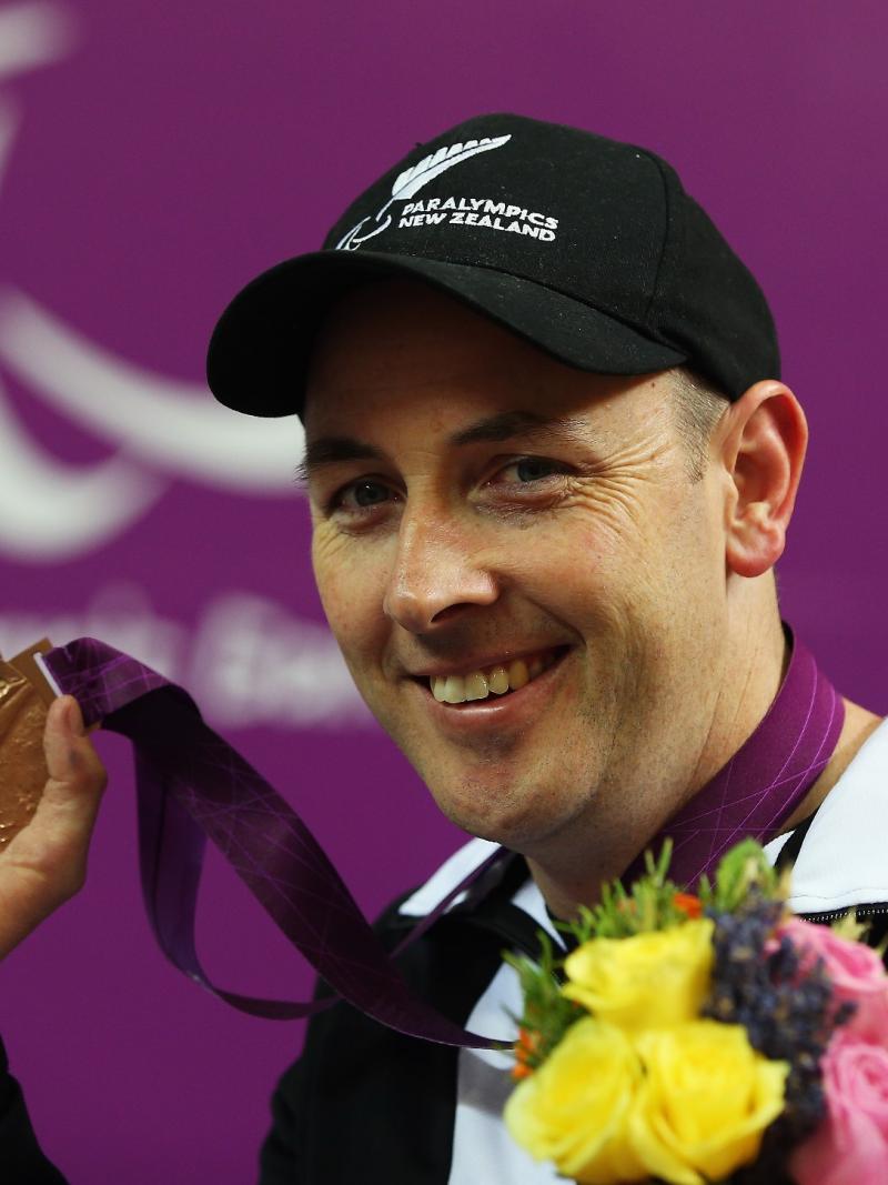 Portrait of smiling man wearing a basecap showing his bronze medal to the camera.