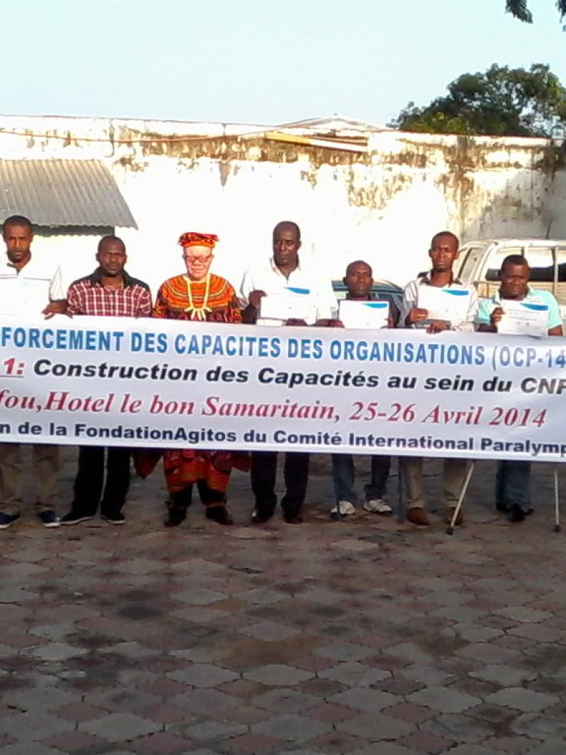 A group shot of people standing and sitting in wheelchairs behind a banner with the following text: Programme de renforcement des capacites des organisations - Niveau 1