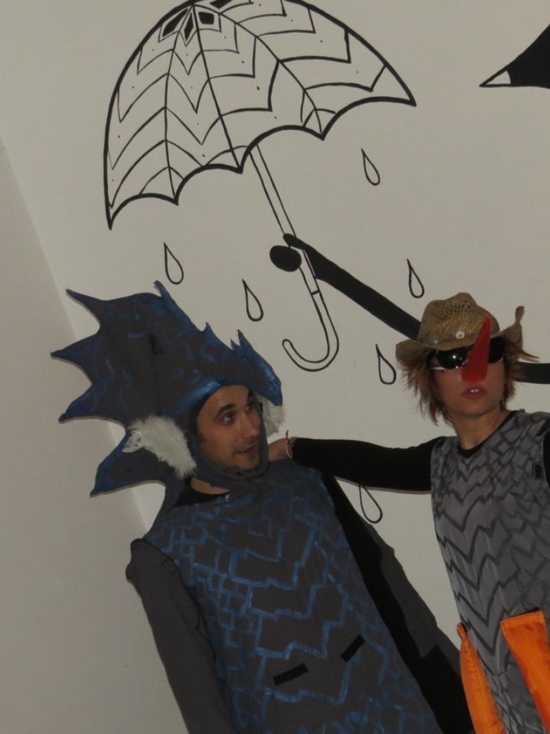 Two persons with a dragon costume stand in front of a wall. An umbrella is painted on the wall behind.
