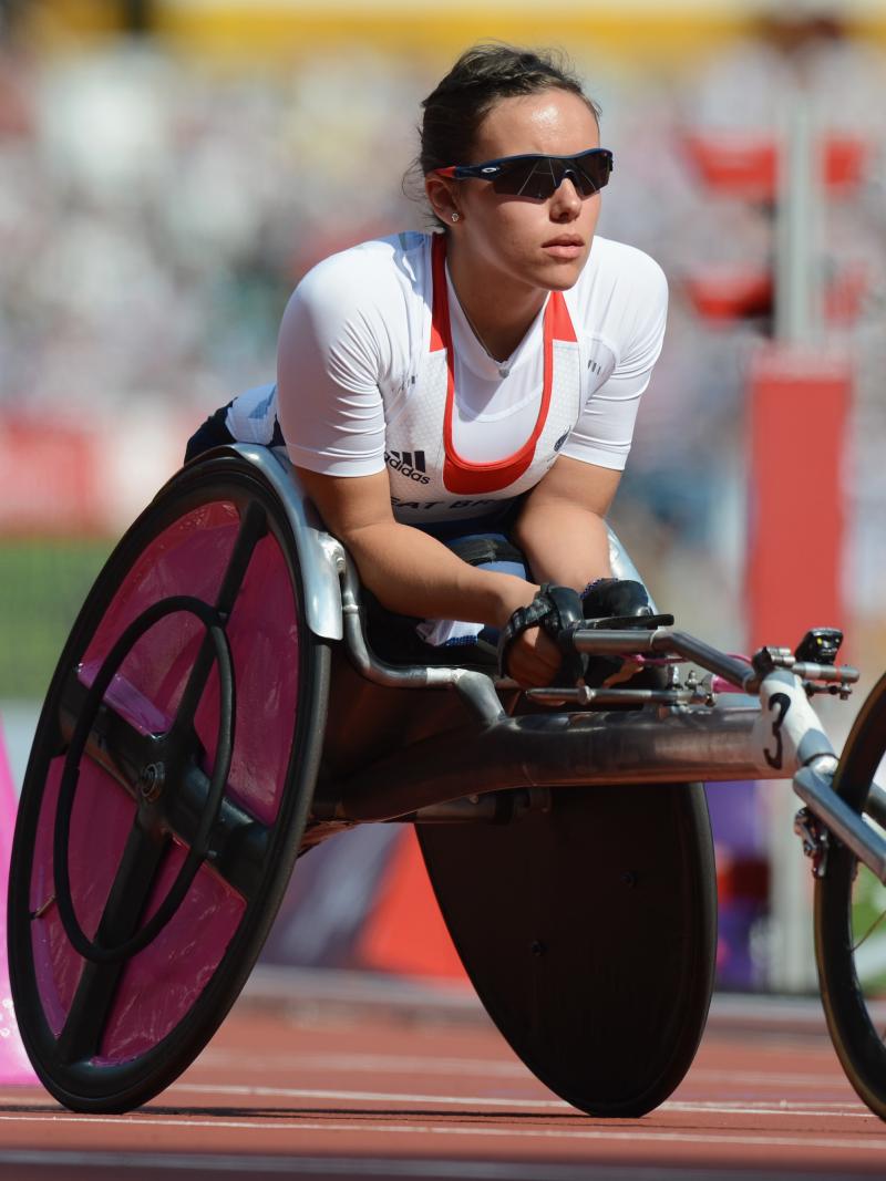 A female wheelchair racer leans forward in her chair wearing sunglasses