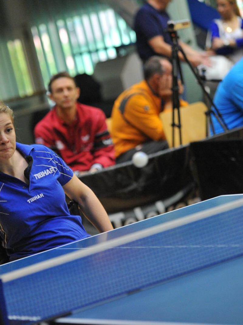 Women in wheelchair in behind a table tennis table batting the ball.