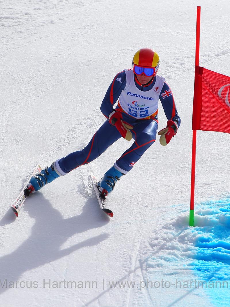 Skier in navy and white ski suit and red helmet skis past a giant slalom gate