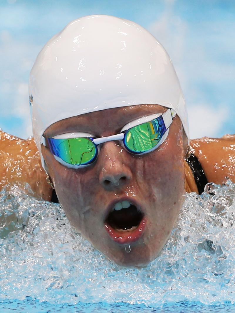 Women wearing swim goggles and a swim cap taking breath while swimming butterfly stroke.