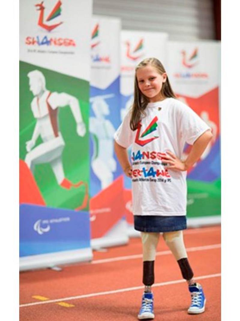 A young amputee girl smiles to the camera, wearing a white t-shirt with a Swansea 2014 imprint