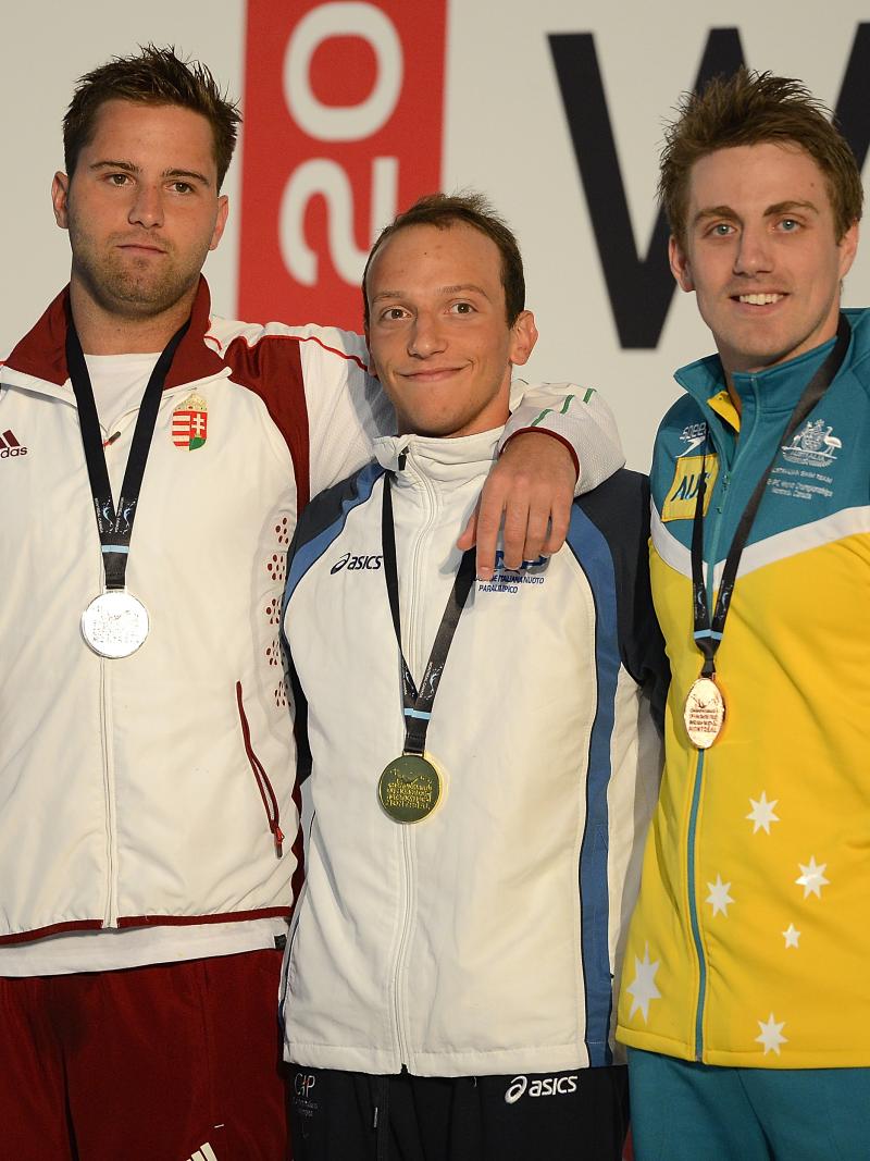 Three swimmers in their team dresses on the podium wearing medals, putting their arms around each other