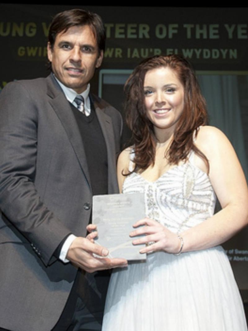 Women and men in dress and suit both hold an award and smile to the camera