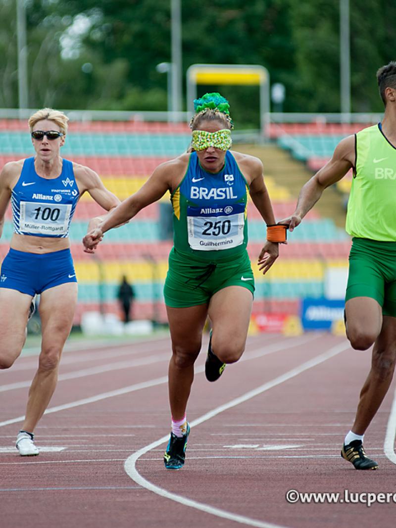 Two blindfolded women running on a track with their male guides. All wearing running suits