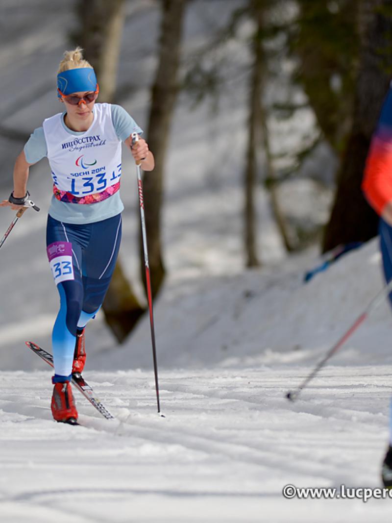 Female cross country skier behind a male cross country skier with orange bib on a track