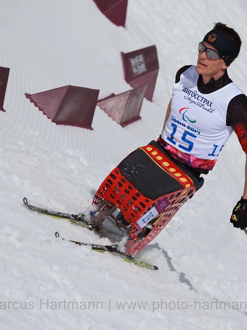 A sit skier rounds a bend in the course in the stadium in Sochi, pushing forward at speed.