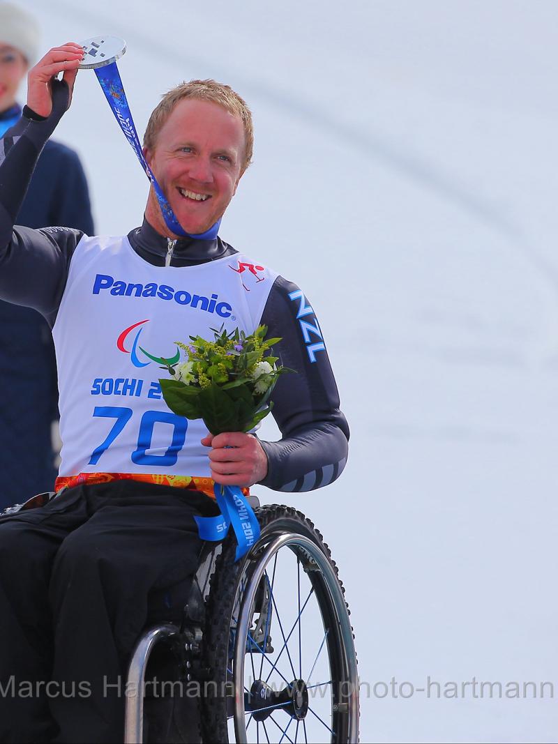 Man in wheelchair on a podium, holding his medal
