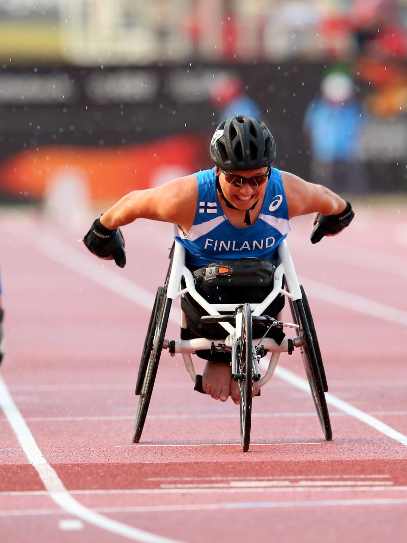 Three wheelchair racers approaching the finish line on the track of a stadium