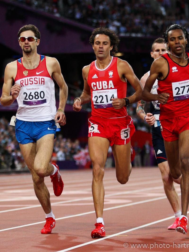Four runners dressed in shorts and vest competing on a red athletics track.