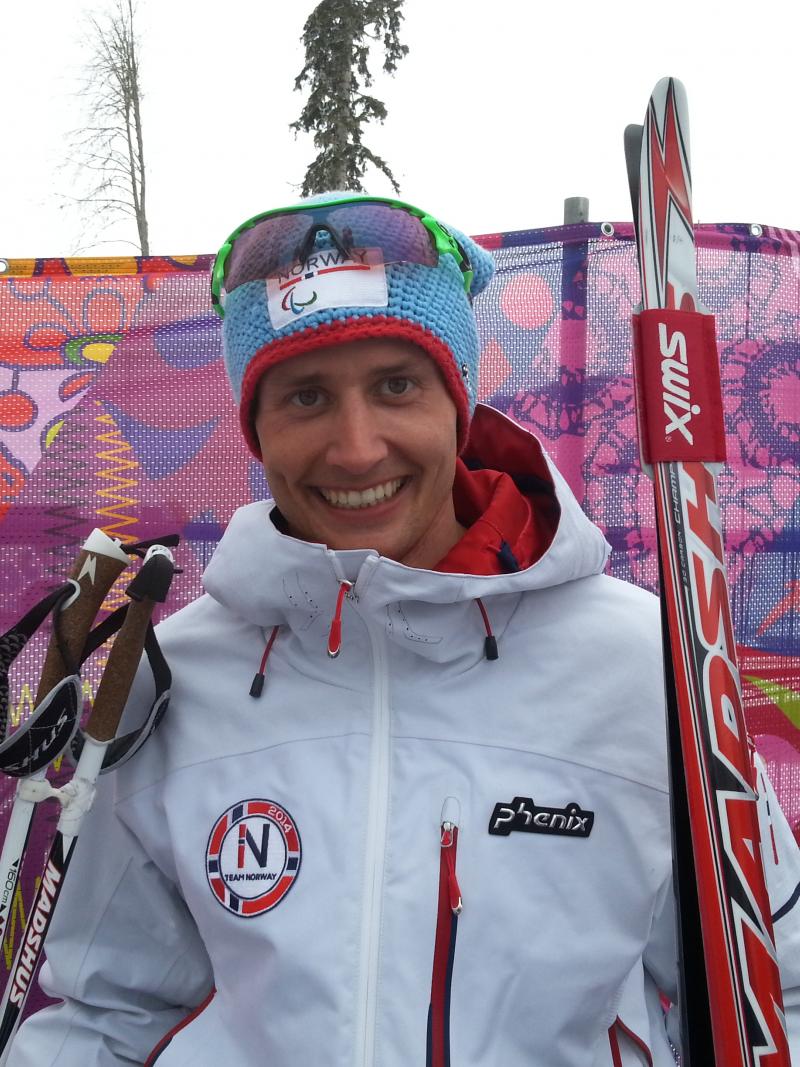 Young man holding cross-country skies smiling to the camera
