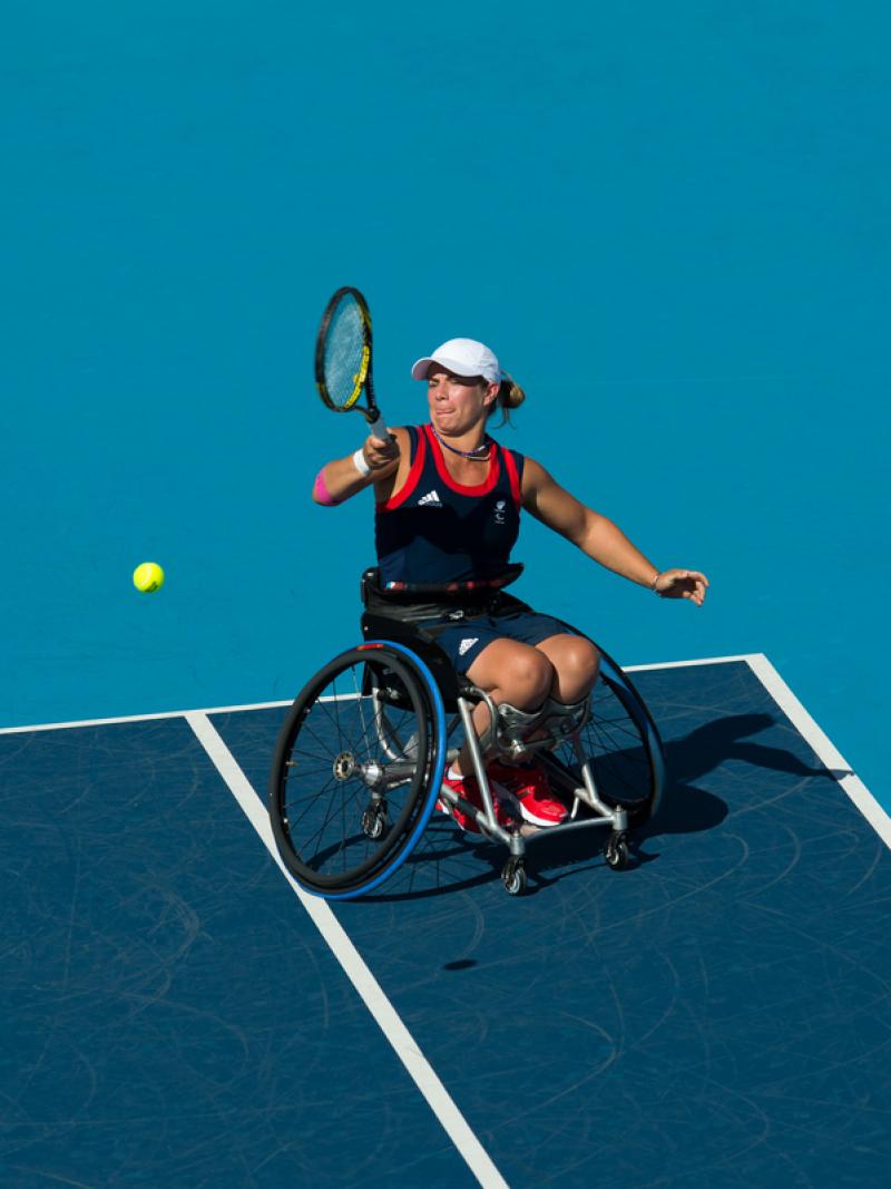 Woman in wheelchair playing tennis on a blue court