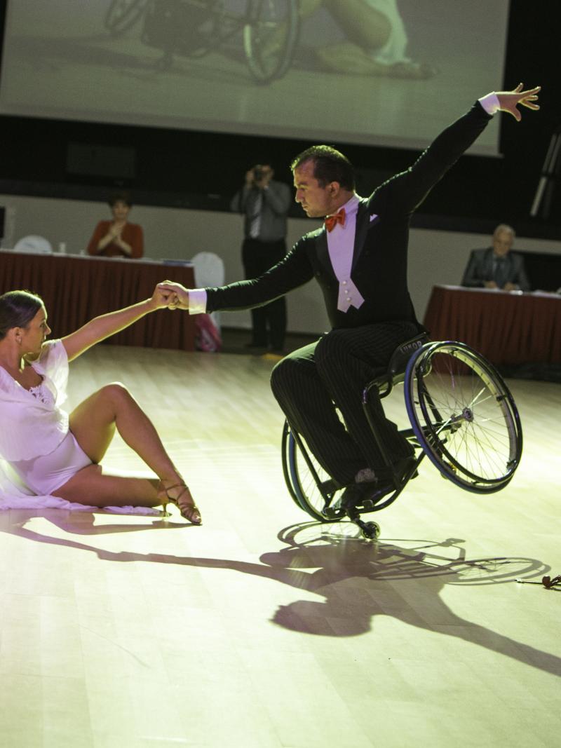 Couple on the dance floow. He is in a wheelchar, she is sitting on the floor, both pose