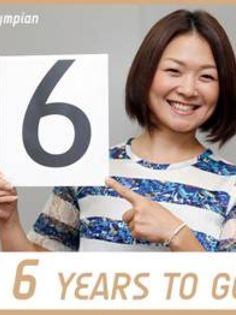 Smiling women holds card with the number six to the camera. Text under the picture says 6 years to go!