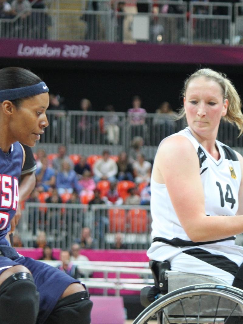 Two women in wheelchairs, playing basketball, fighting for the ball