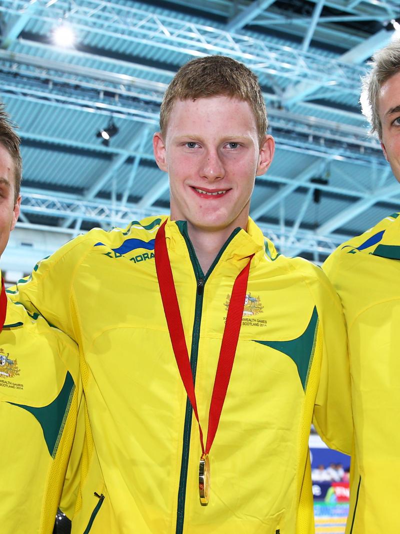 Three swimmers show their medals to the camera and smile