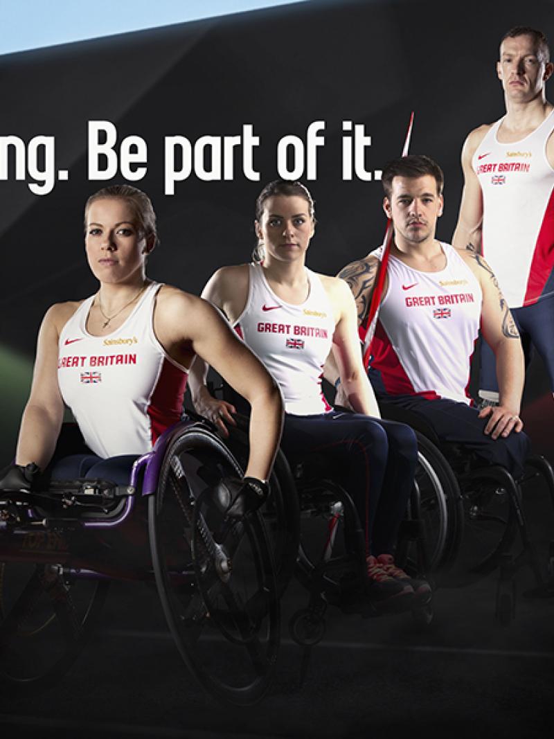 5 male and female athletes in British jerseys stand and sit (in wheelchairs) next to each others in front of a black wall. Behind them is the logo: Swansea 2014. It's coming. Be part of it.