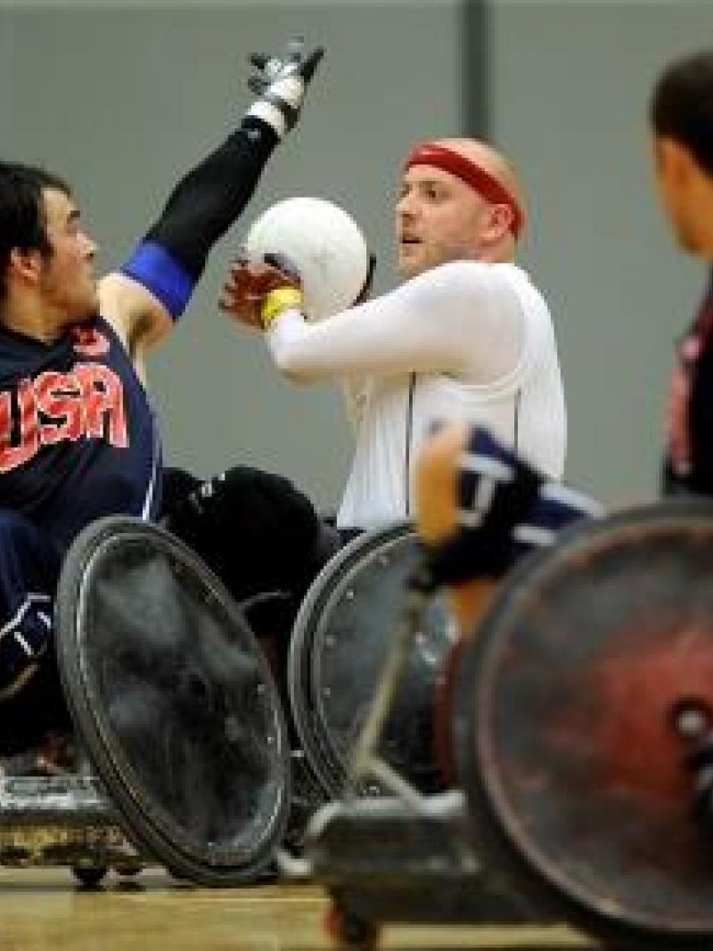 Two wheelchair rugby players fight for the ball on the field of play